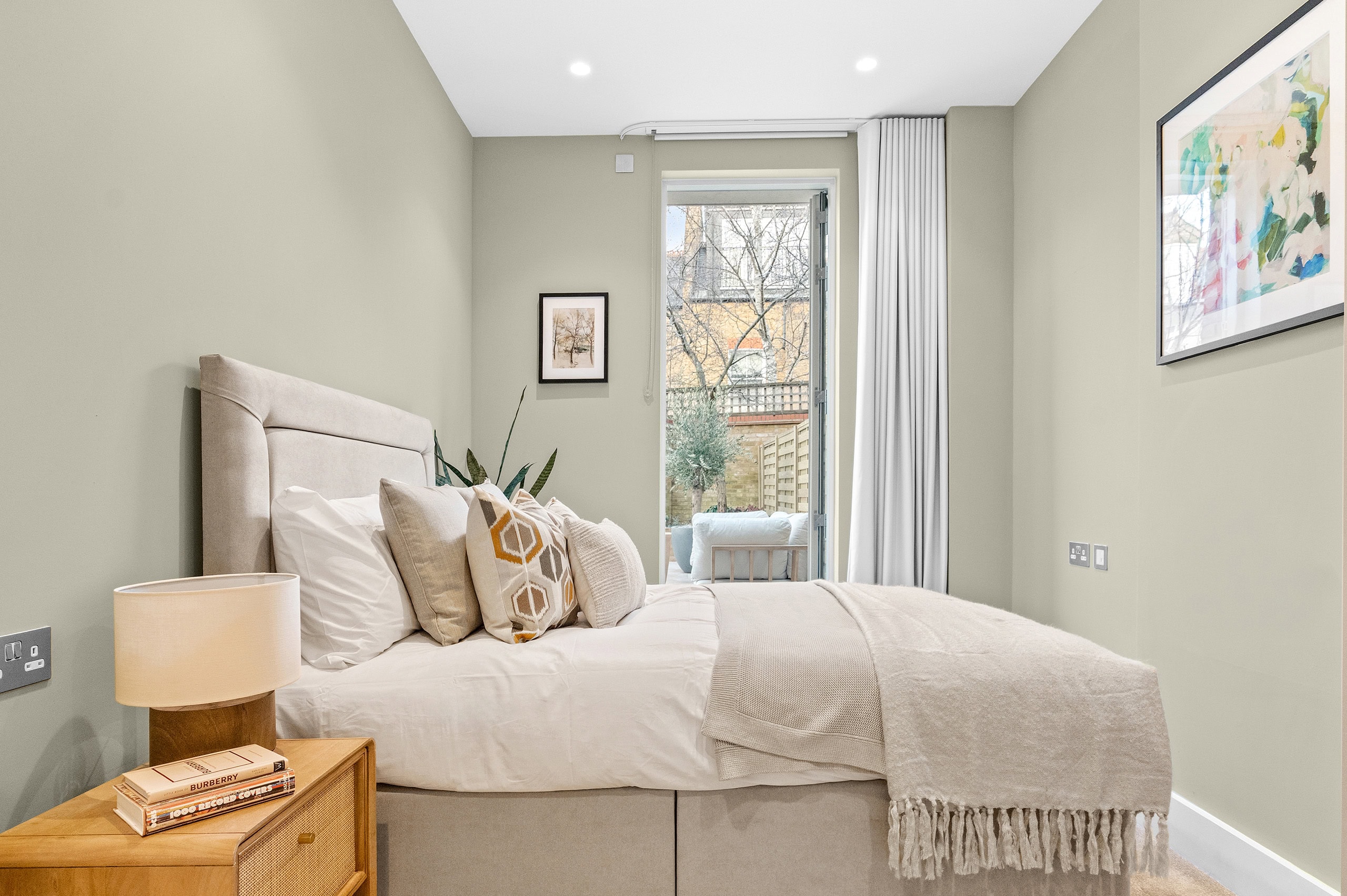 Well-lit bedroom looking towards bedside cabinet bed and window from the side.