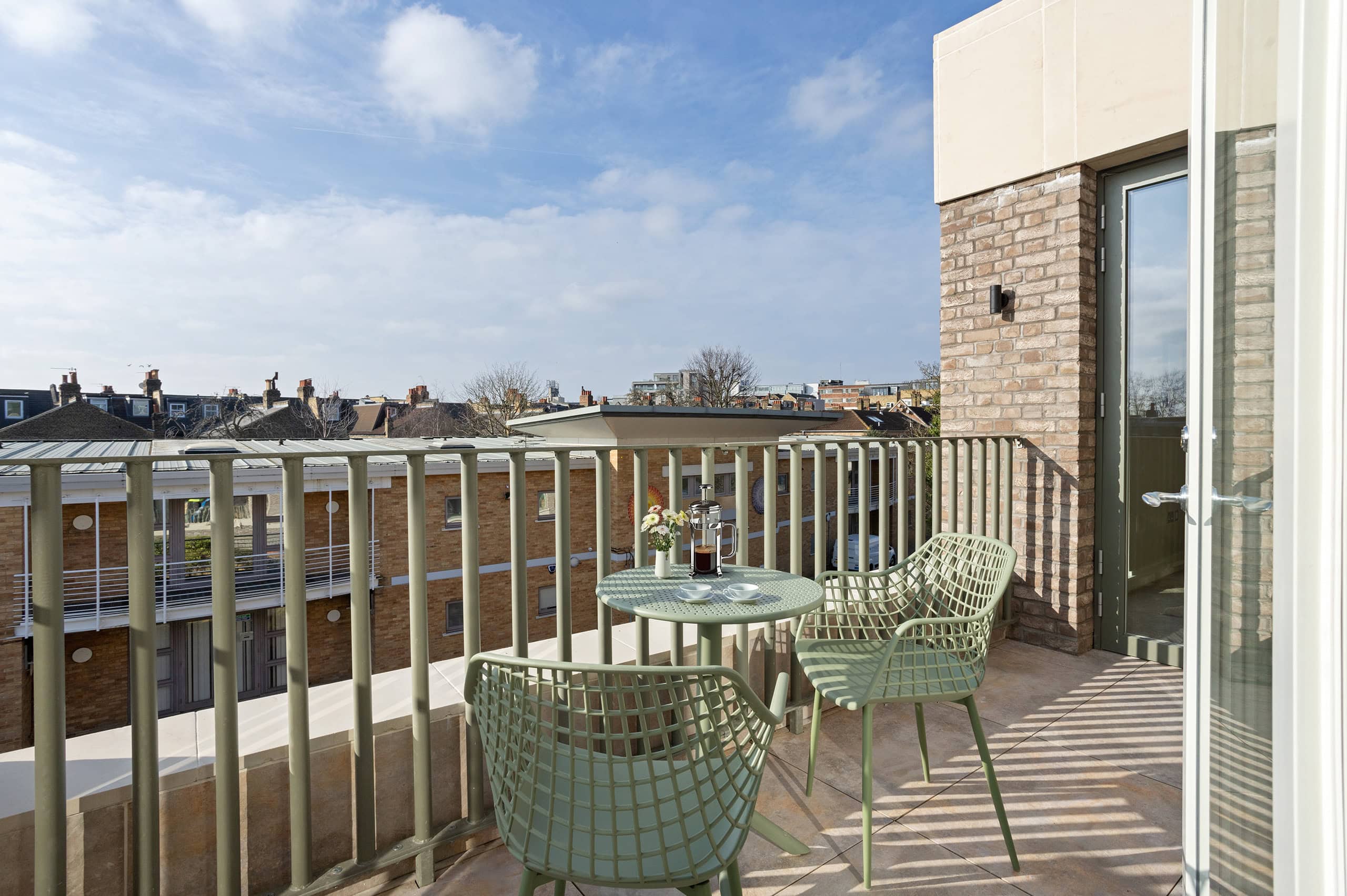 View from balcony on a sunny day looking over green railings towards the distance. Two green chairs on the balcony