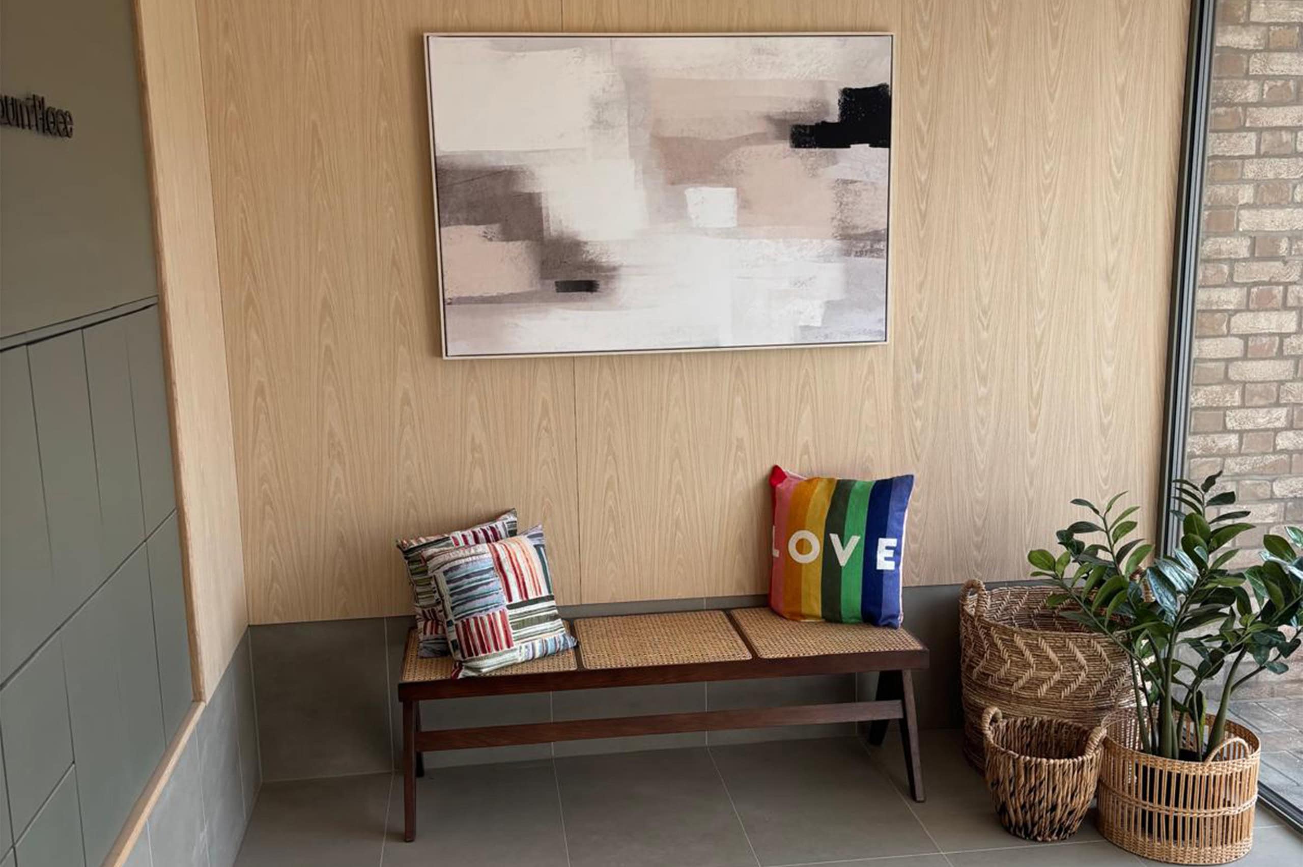 bench decorated with cushions against a beige wall with two potted plants to the right hand side