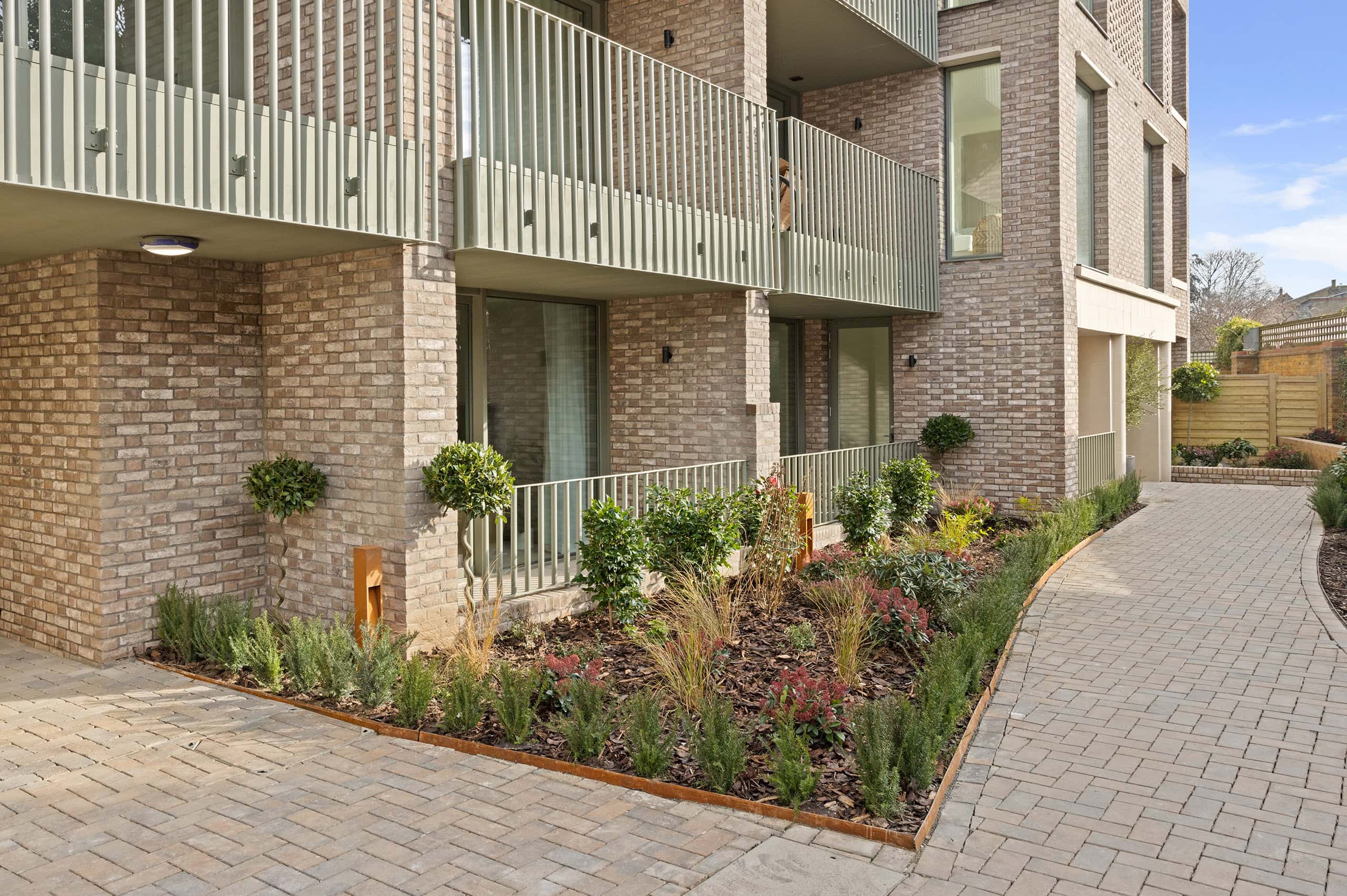 View of the development from outside, with 1st floor balconies visible. A small plant garden in front of the building